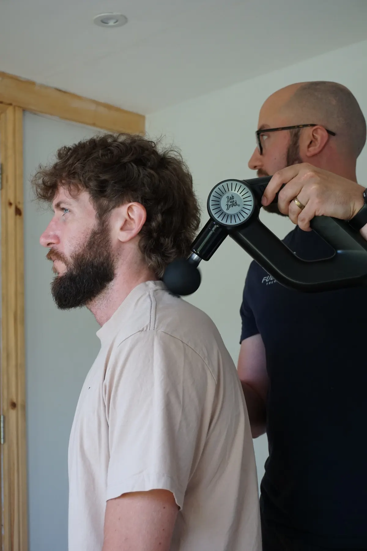 Rob using a percussion massage device on a client's neck and shoulders